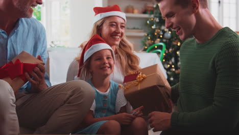 Una-Familia-Multigeneracional-Celebra-La-Navidad-En-Casa-Con-Gorros-De-Papá-Noel-Y-Astas-Abriendo-Regalos