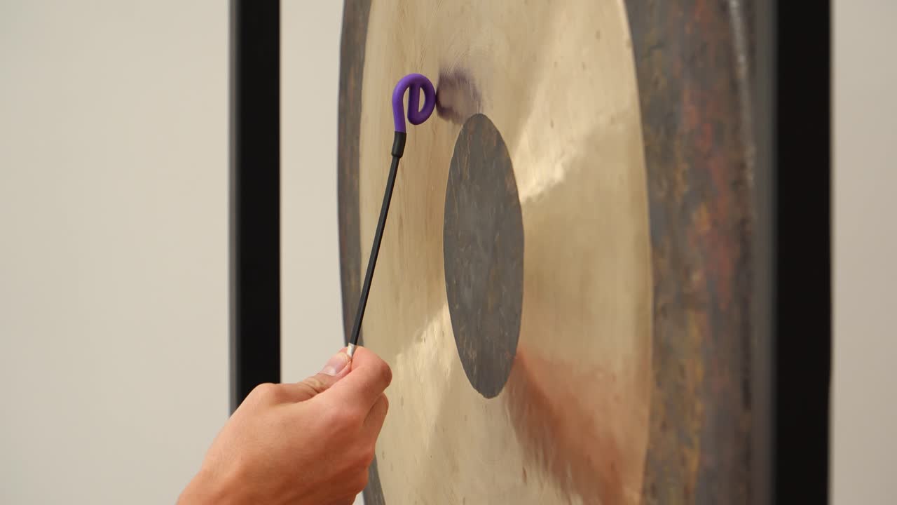 Tight side detail of a rubber friction mallet ring rubbing a large symphonic gong to produce sustained singing tones in a calm minimalist indoor studio