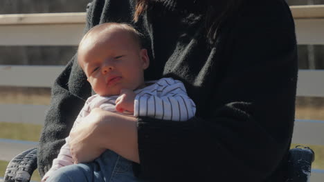 Portrait-of-young-baby-in-mothers-arms-under-outdoor-sunlight