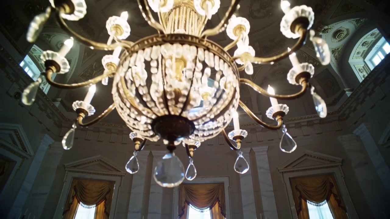 Telecamera che sale, rivelando un lampadario dorato in una sala a cupola, mostrando dettagli in cristallo.