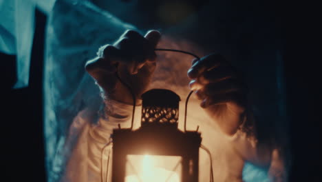 hands holding a glowing antique lantern in darkness