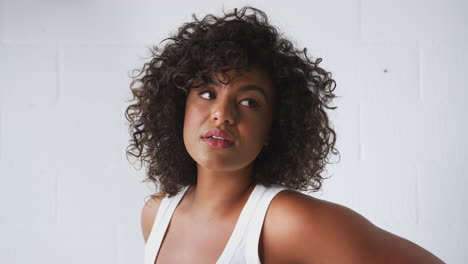 Retrato-De-Una-Mujer-Sonriente-Vestida-Informalmente-Con-Un-Chaleco-De-Pie-Contra-La-Pared-De-Un-Estudio-De-Ladrillo-Blanco