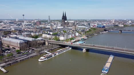 Cologne-city-center-in-Germany,-Aerial-dolly-out-over-river-Cruise-ship,-Cargo-Barge-and-public-transport-traffic-on-deutzer-bridge-and-Cathedral