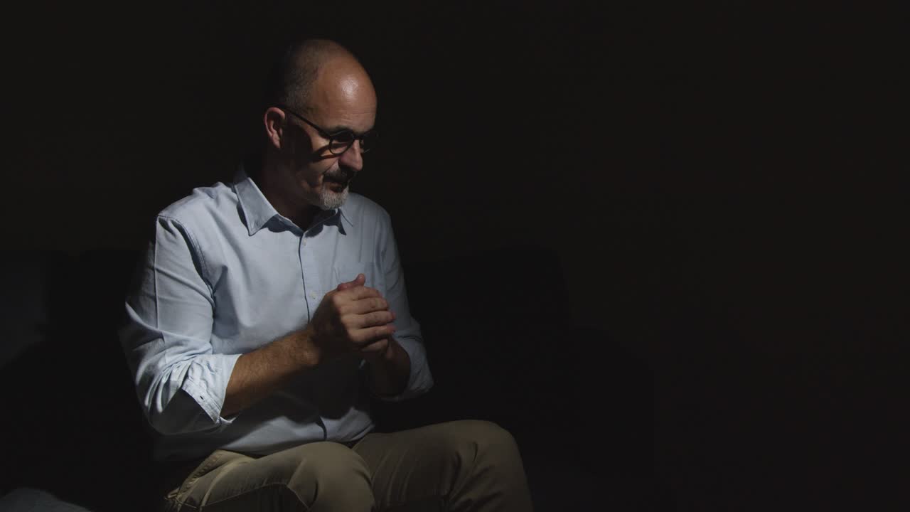 hombre maduro deprimido luchando con la salud mental sentado en la oscuridad en el sofá con iluminación baja 8