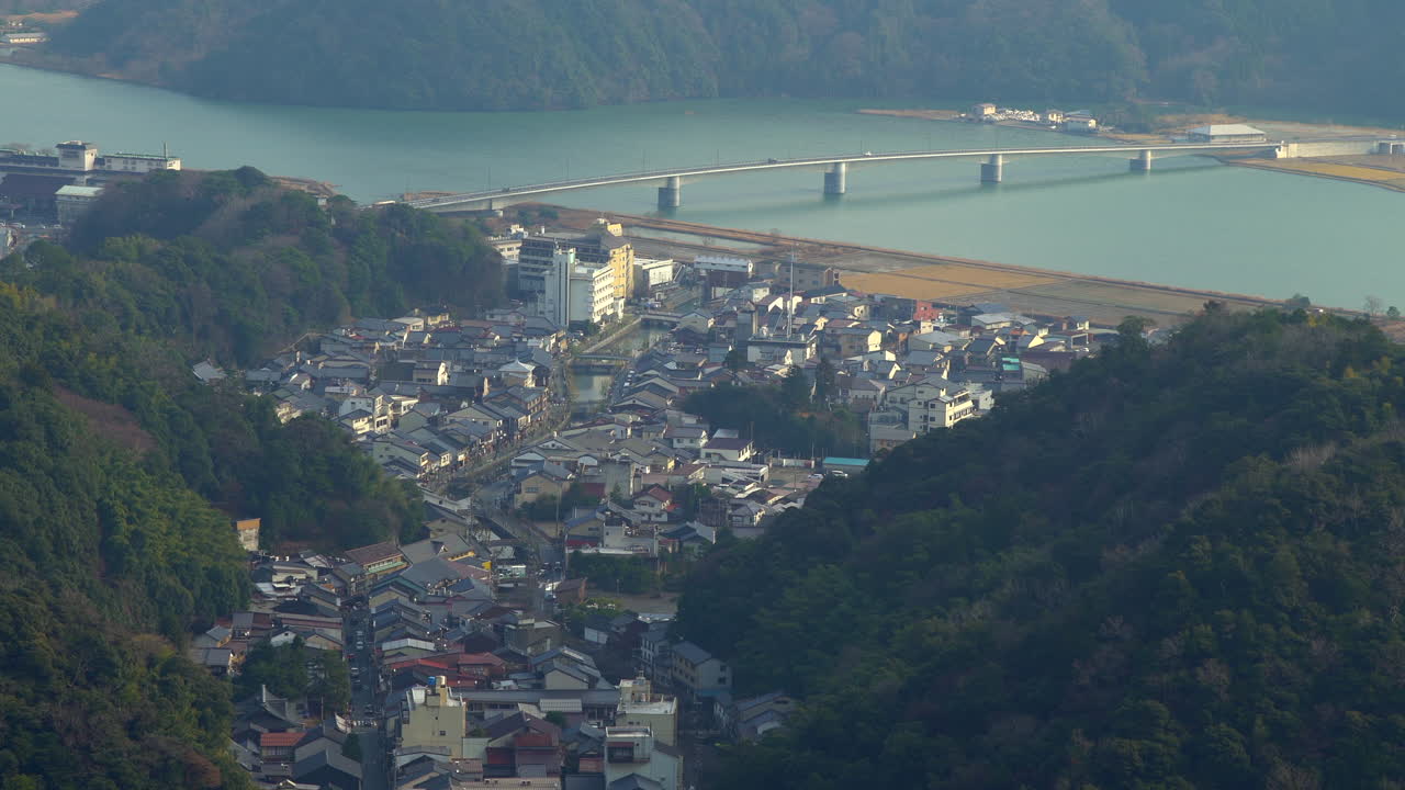A zoomed-in aerial perspective of Kinosaki Onsen's traditional buildings and Kinosaki bridge nestled in a mountain valley. Filmed in Hyogo Prefecture, Japan