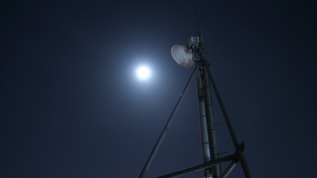 A captivating timelapse of the moon setting behind a communication tower, with clouds moving in the background, creating a dramatic celestial scene.