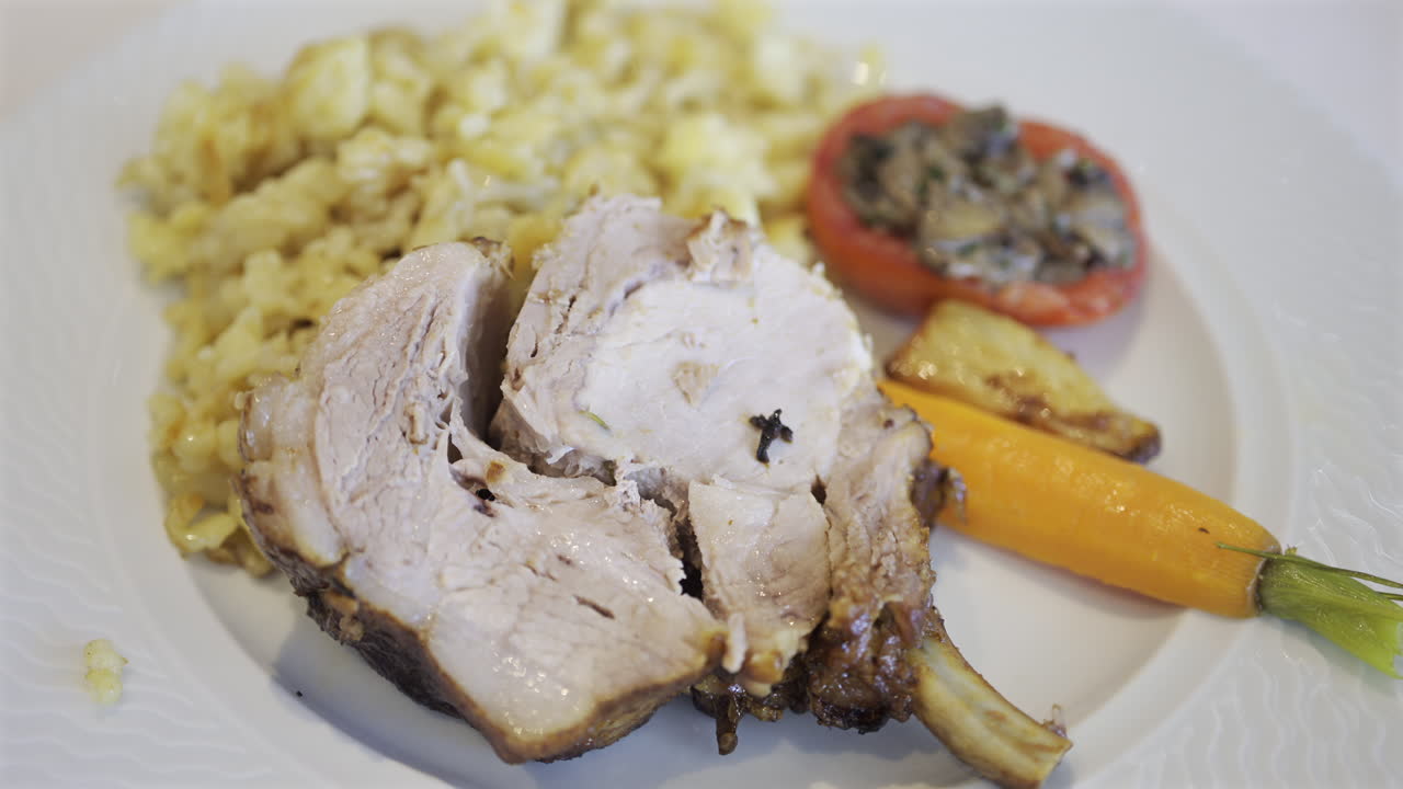 Close up of a server arranging a portion of egg noodle near a few pieces of pork, cooked carrot and stuffed tomato on a white plate
