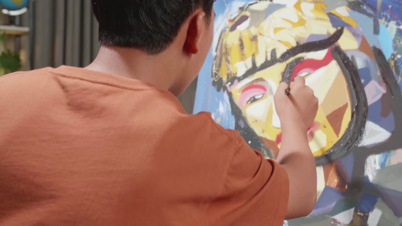 Hind View Of An Asian Artist Boy In Wheelchair Holding Paintbrush And Painting A Girl'S Face On The Canvas