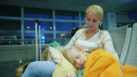 a woman is stroking a girl sleeping on her lap sitting in the terminal of the airport flight delay c