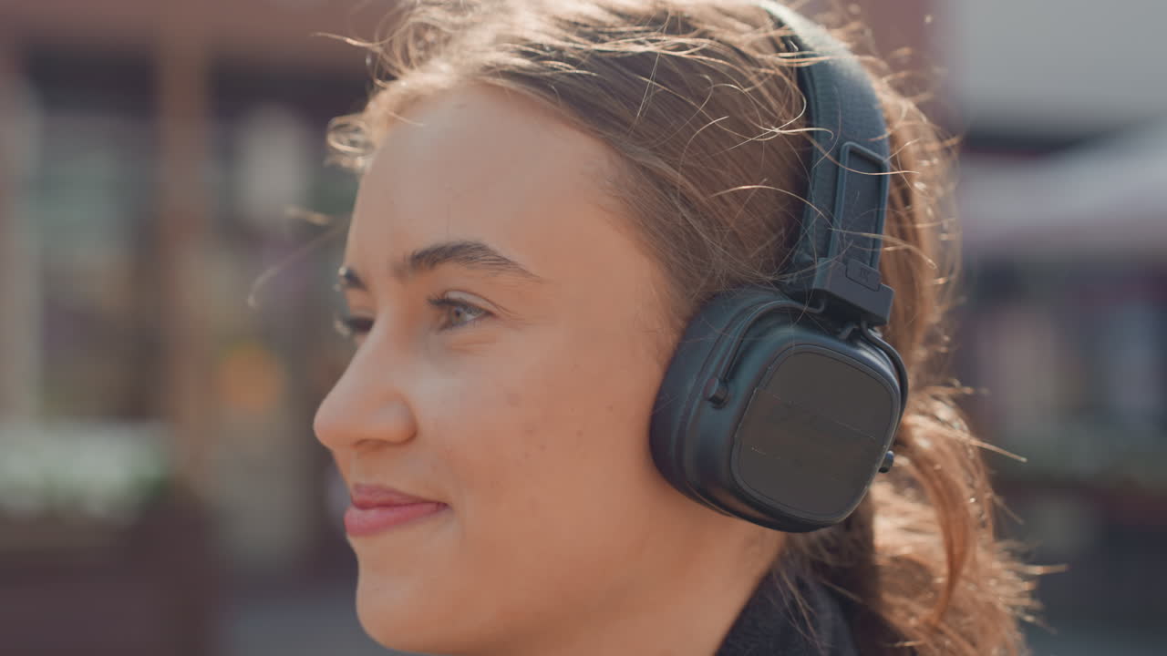 Donna che si gode la vita all'aria aperta, signora caucasica che si delizia con bevande e musica fuori, all'aria aperta, donna con cuffie wireless che sorride serenamente mentre cammina attraverso un vivace mercato all'aperto