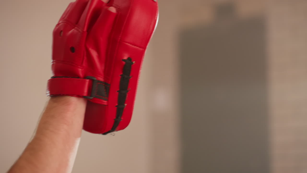 Closeup of red boxing pad on trainer hand used during boxer workout, showing equipment details, stitching, strap, and grip essential for combat sports training, practice, and preparation