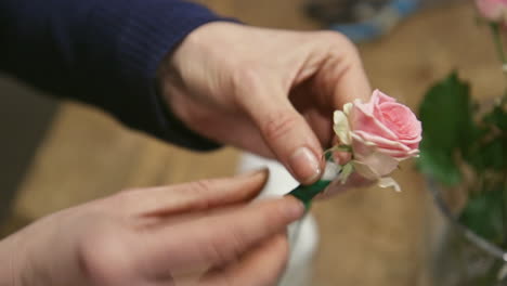 skilled florist preparing rose with wet cotton for flower bouquet