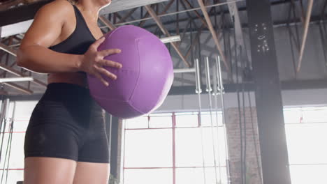 holding purple medicine ball, woman exercising in gym for fitness training