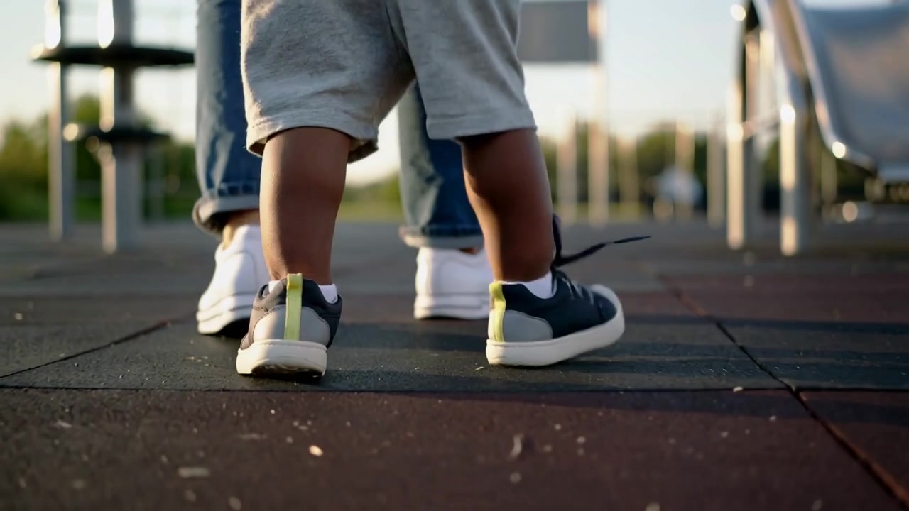 Walking toddler following adult stepping balancing on park rubber tiles in navy and white sneakers