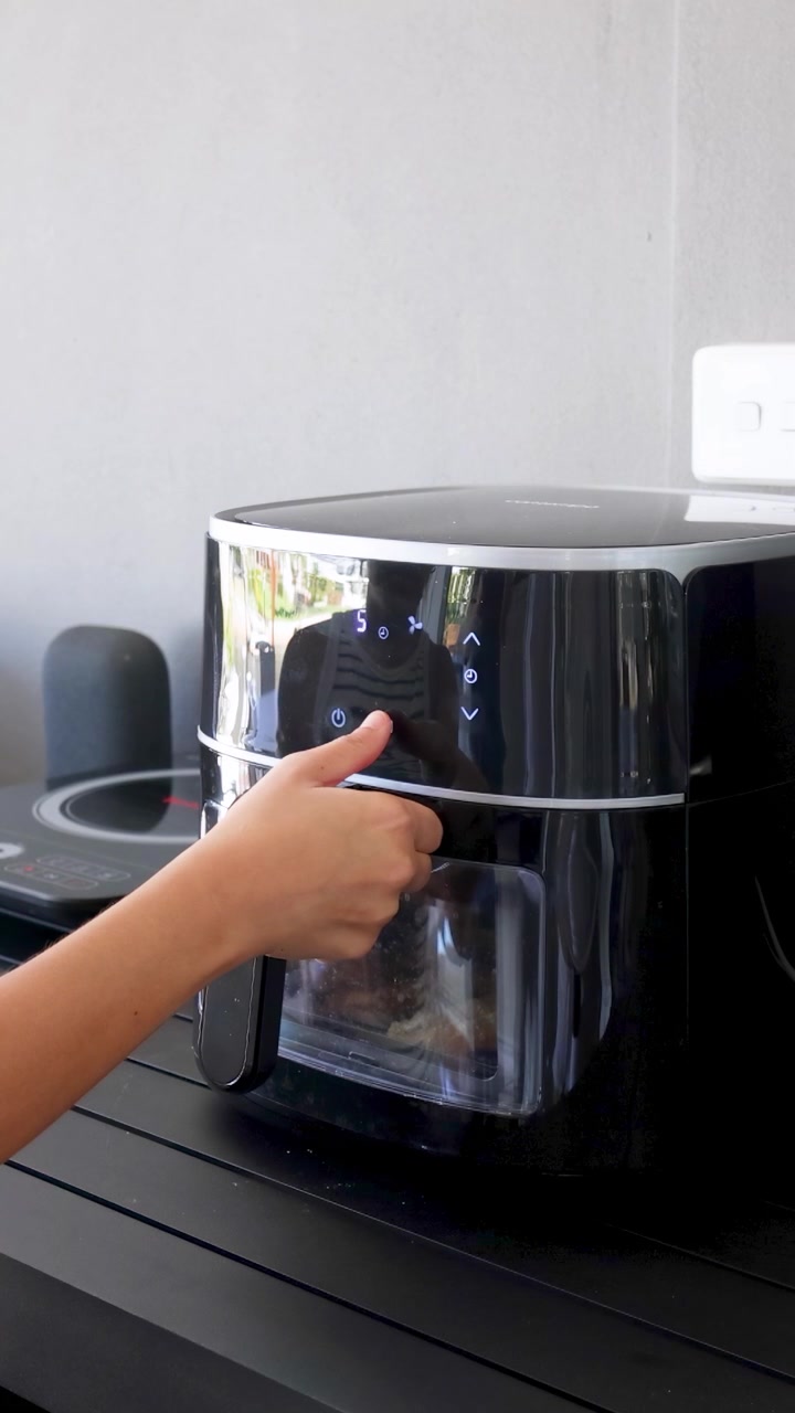 Una persona opera una freidora de aire, ajustando la configuración y revisando la comida en un entorno de cocina elegante y moderno