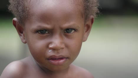 close up shot, indigenous kid waving and smiling, curled hair. poverty concept.