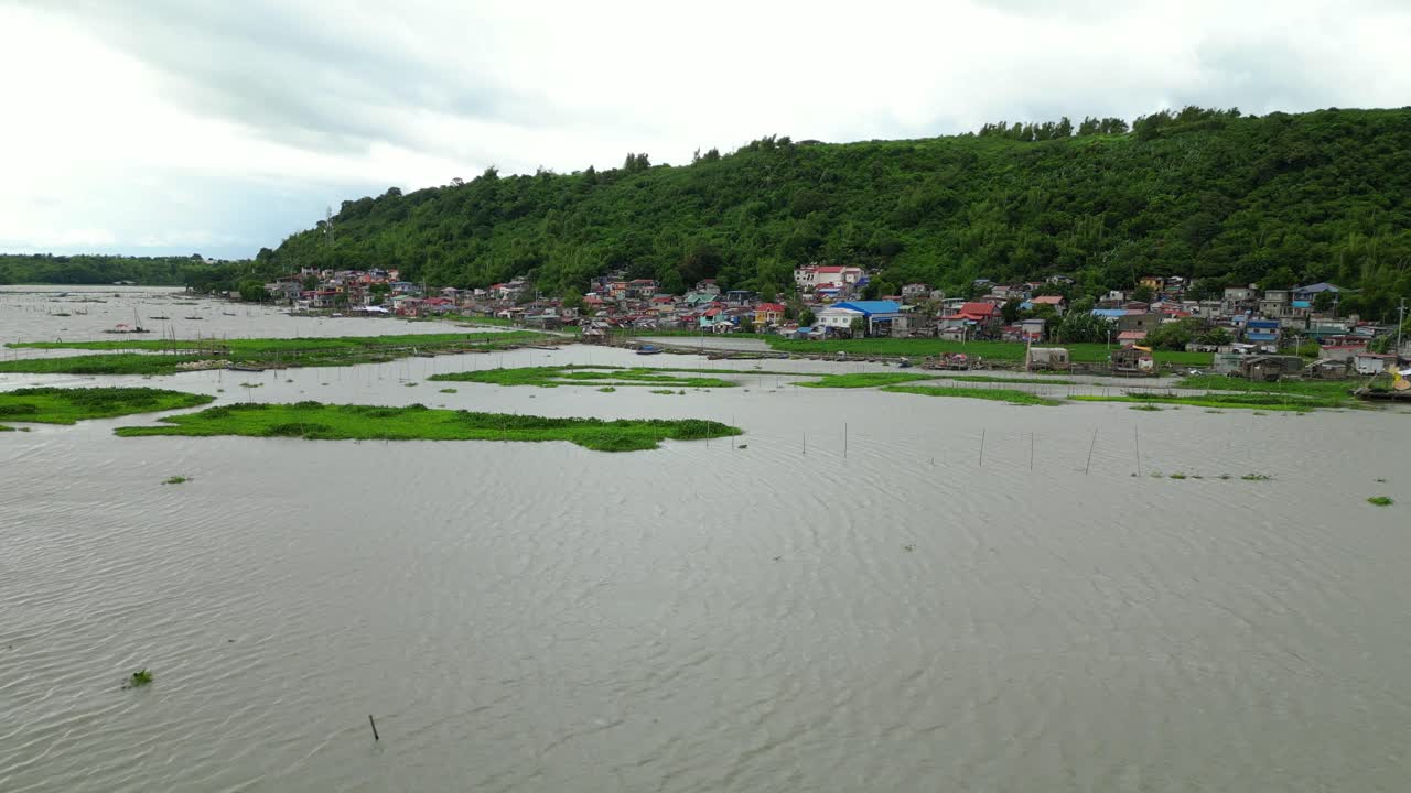 Aerial view captures a riverside community in the Philippines, with docked boats, colorful homes, and lush greenery surrounding calm waters