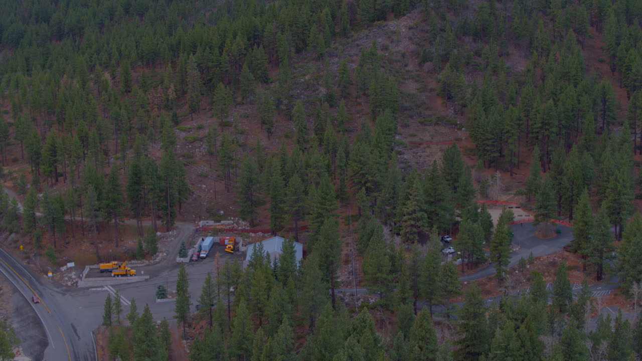 View of mountainside covered in Douglas Fir trees in Lake Tahoe, Nevada with tilt down to reveal road below with car driving past
