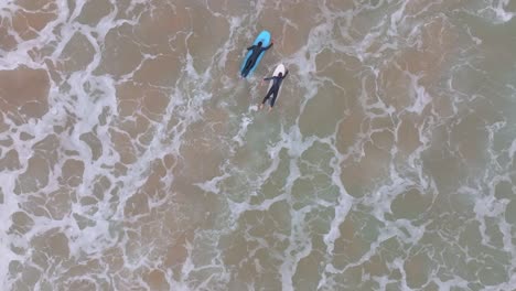 top down tracking view of two longboard surfers paddling out to catch ocean wave