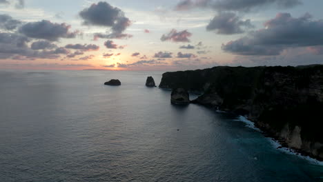 escarpment drop off cliffs of nusa penida bali with setting sun below horizon