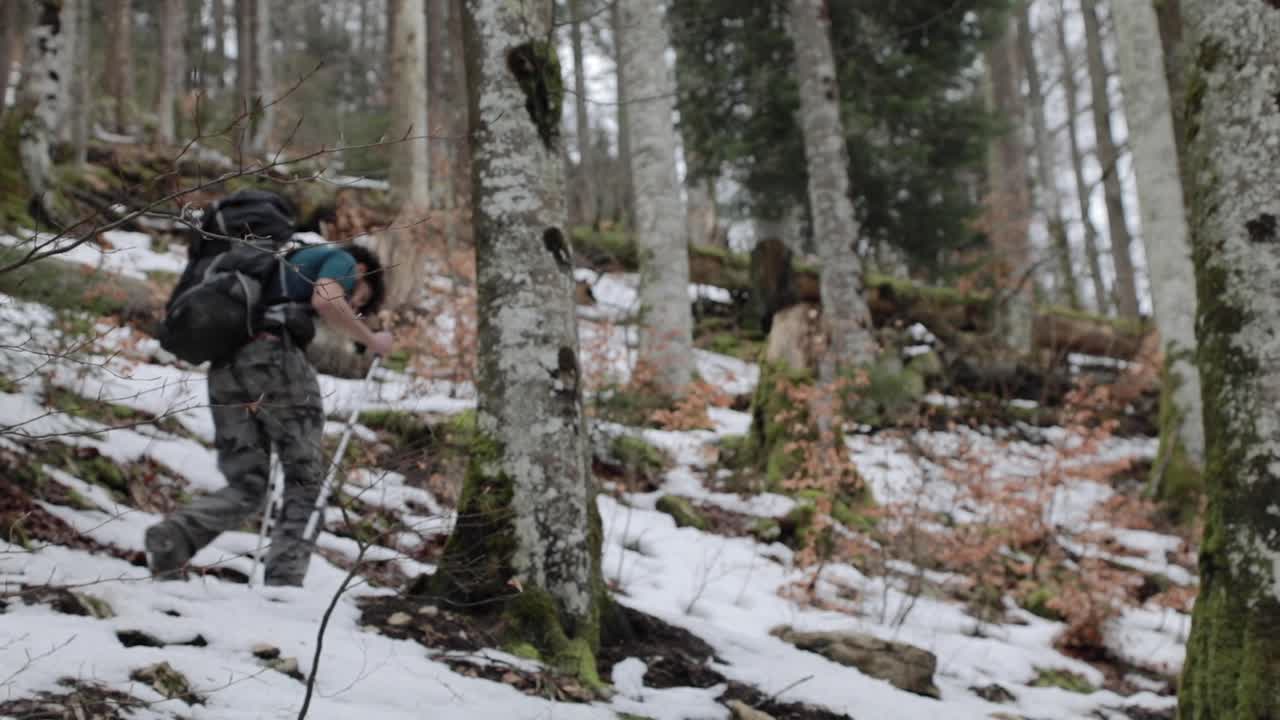 Backpacker man hike alone through winter snow covered forest steep hill. Slowmo