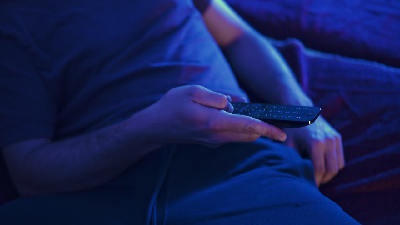 Ripresa a mano di un uomo che riposa sul divano e cerca il telecomando TV.