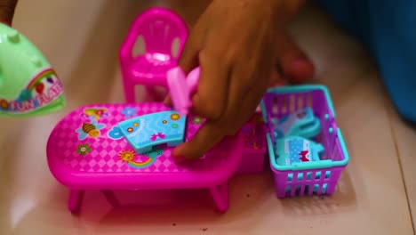 a pretty little girl plays a housewife, ironing children's clothes with a toy iron