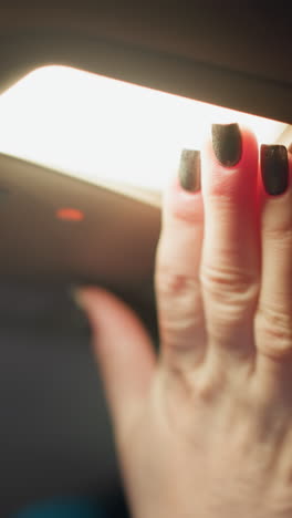 vista en primera persona de una mujer encendiendo la luz del coche por la noche. su mano con uñas pintadas de negro es claramente visible mientras alcanza el interruptor de la luz dentro del coche