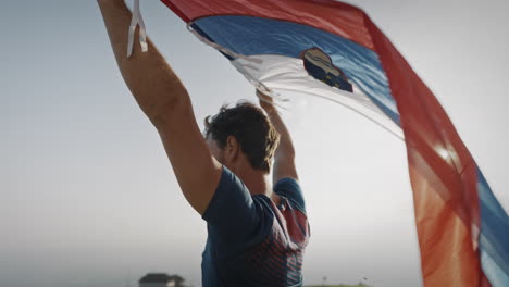 Hombre-Sosteniendo-Una-Bandera-Eslovena-Sobre-Su-Cabeza-Para-Dejarla-Ondear-En-El-Viento