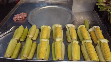 close up shots of yellow corn place on top of a metal steamer showing that it hot with one hand, a tong and piece cloth