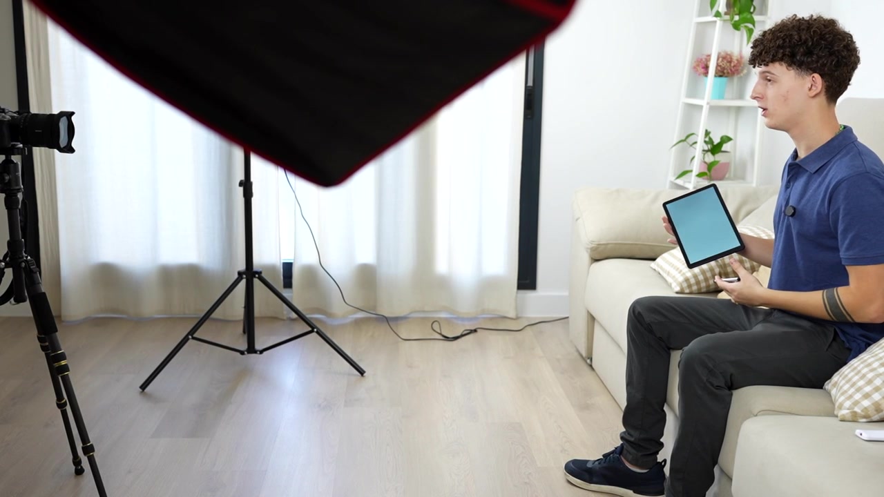 Young influencer sitting on a sofa while recording a tablet review for his social media channel