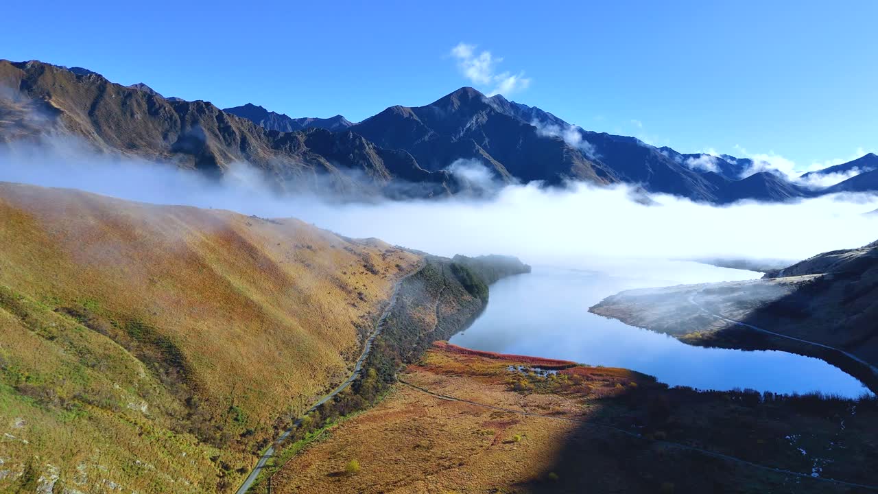 Aerial footage of Moke Lake surrounded by misty mountains in Queenstown, New Zealand, under clear blue skies
