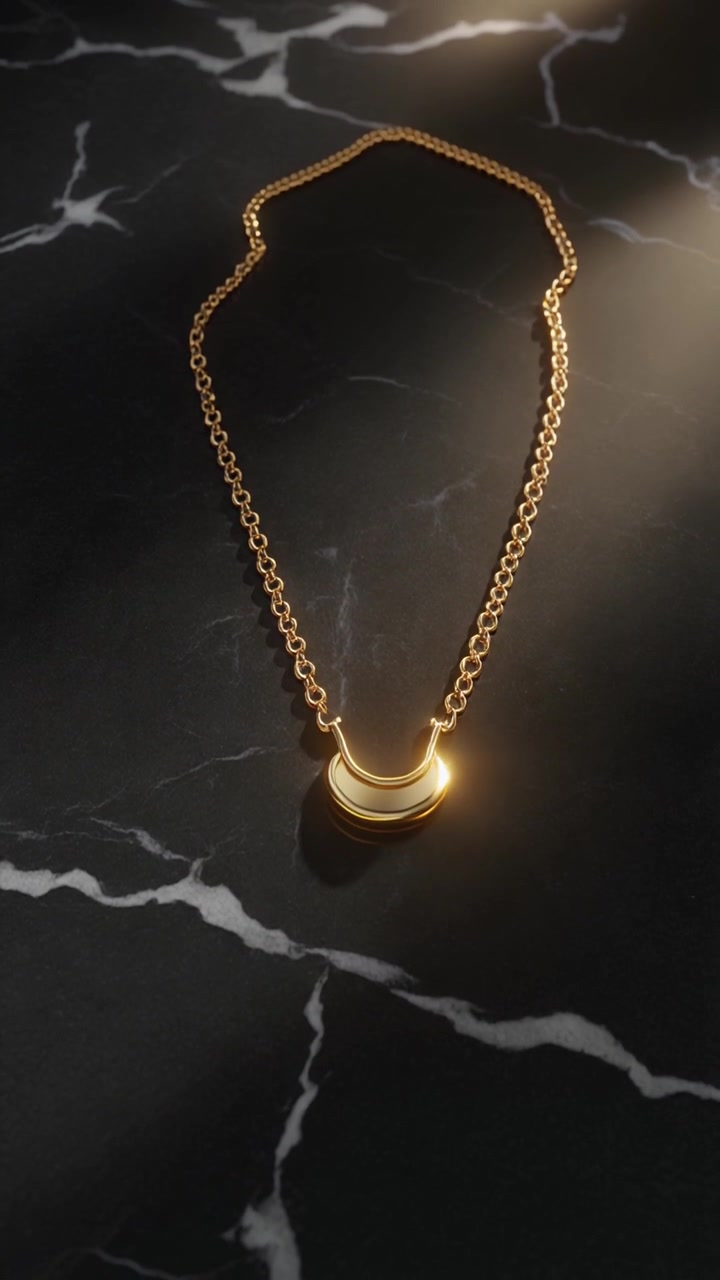 Una delicata collana a catena in oro con un ciondolo a mezzaluna poggia su una superficie in marmo nero con una calda luce solare