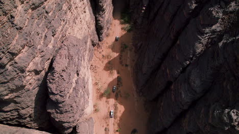 aerial view of off-road suv cars driving between the sandstone cliffs in tassili n'ajjer national park in djanet, algeria