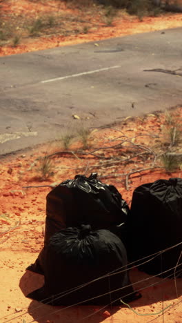 three black garbage bags sit on a dirt road in the australian outback