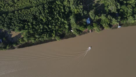 Toma-Aérea-De-Arriba-Hacia-Abajo-Del-Barco-Que-Navega-En-El-Río-Amazonas-De-Color-Marrón-Y-Que-Llega-Al-Muelle-En-El-Bosque