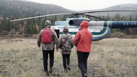 people walking towards a helicopter in a mountainous forest landscape