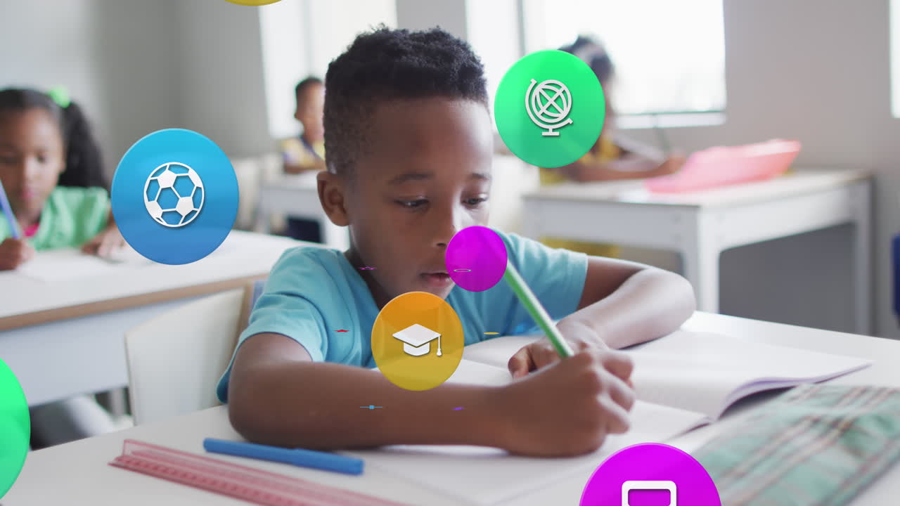 Animation of school icons over busy african american schoolboy working at desk in class