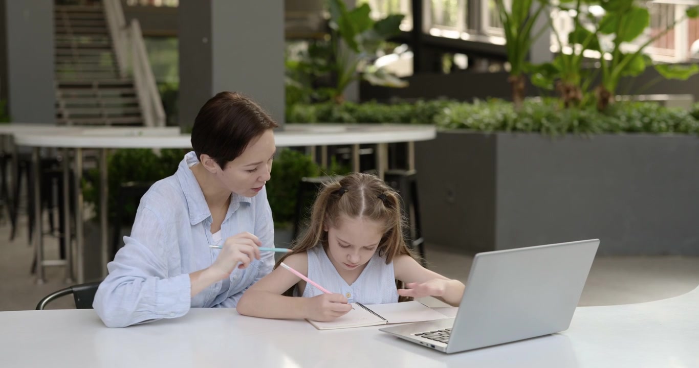 Donna che aiuta una giovane ragazza con i compiti usando un laptop e un quaderno