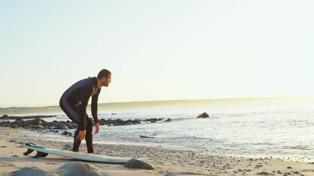 해변에서 서프보드 리쉬를  ⁇ 는 중성인 백인 남성 서퍼의 측면 뷰 4k