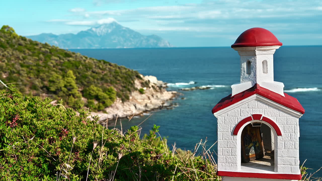 An old and small shrine located on the Aegean sea coast, bushes around, water and mountains on the background, Greece