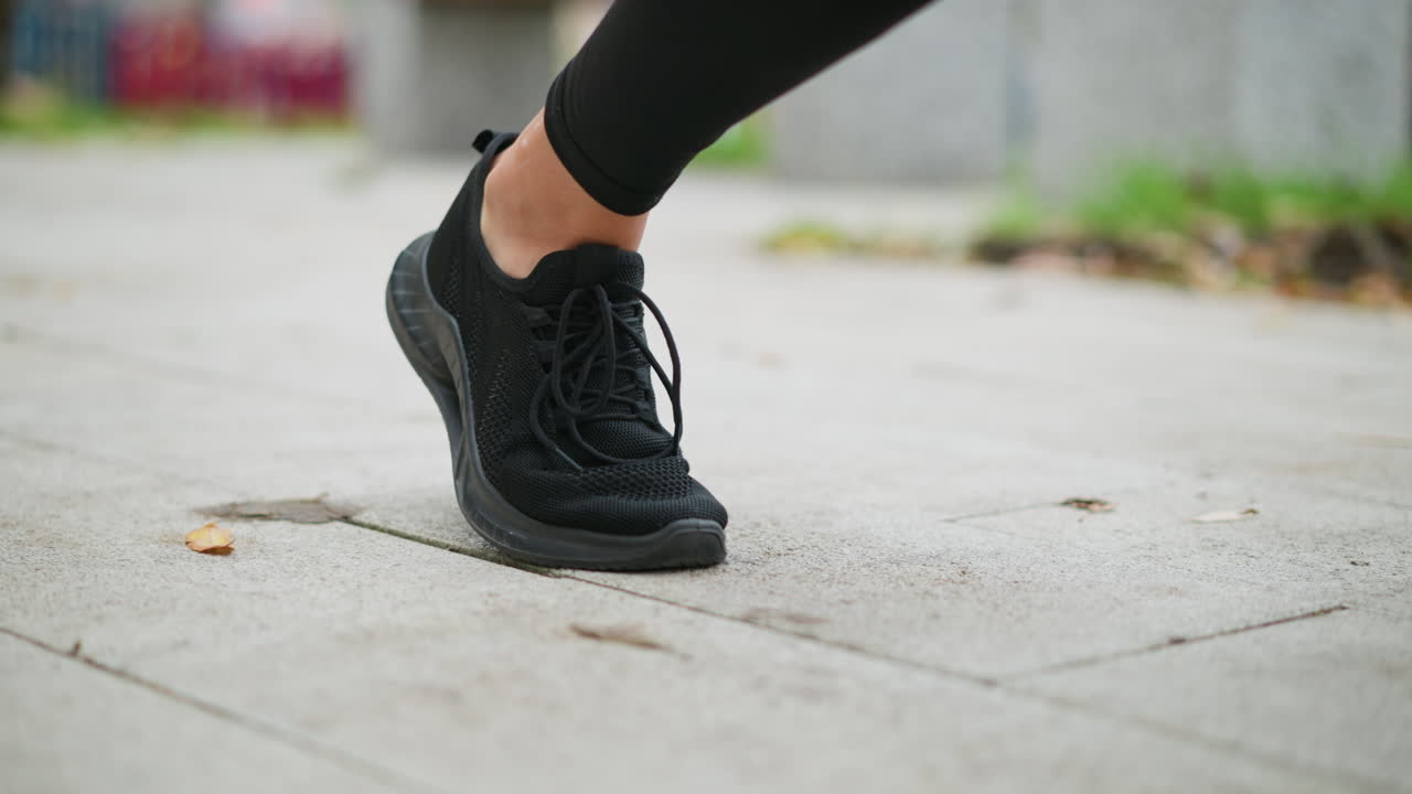 Close-up view of runners leg in black sneakers, stretching out ready to move, on a smooth paved path with blurred natural background, preparing for a run or jog