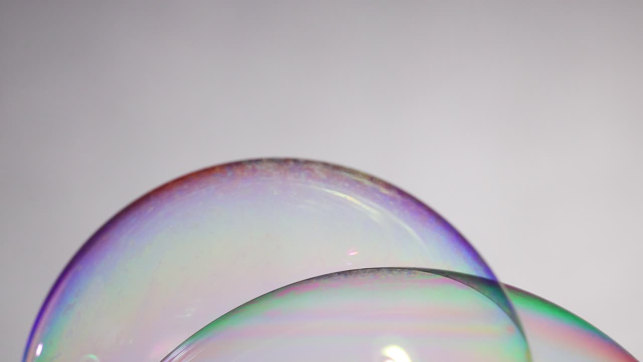 Vibrant soap bubbles display shifting colors and reflections against a neutral background, captured in a smooth, flowing sequence