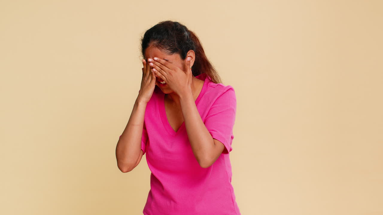 Indian woman emotionally covers face with hands showing sadness looking sadly through fingers