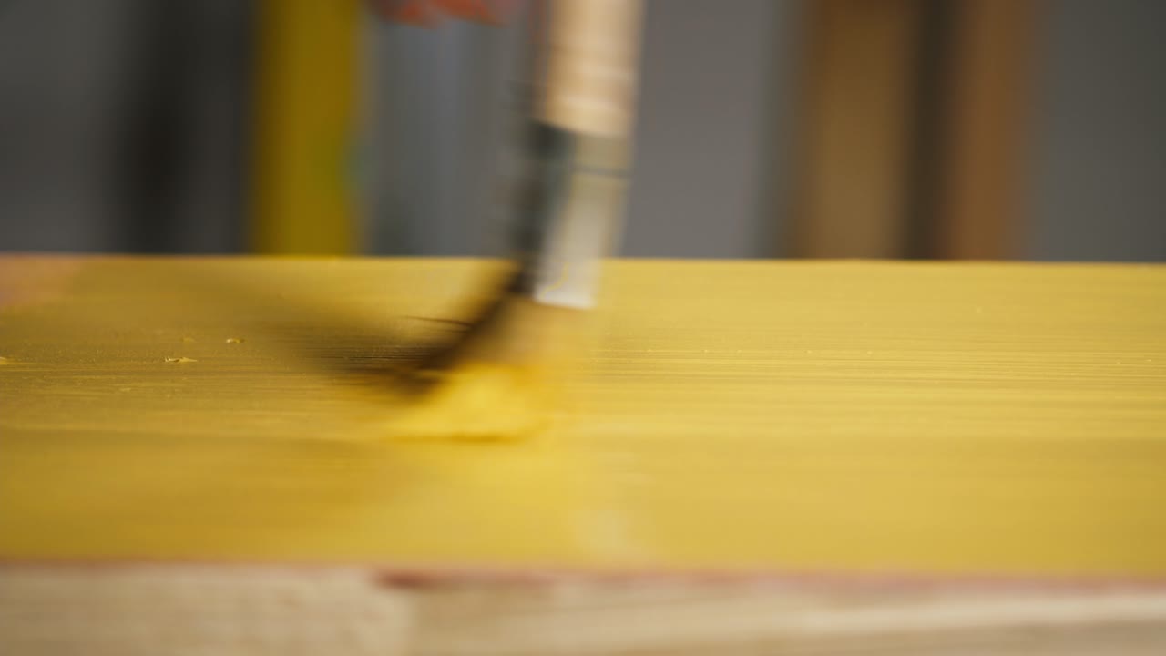 Primo piano di una mano che dipinge una superficie di legno con un pennello giallo