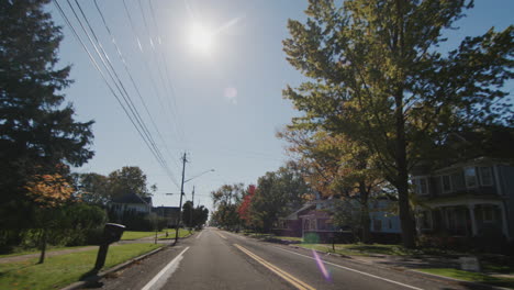 drive along a typical american town on a clear autumn day. the sun illuminates houses and trees beautifully. rear view