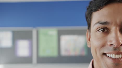 Portrait-of-happy-biracial-male-teacher-smiling-in-classroom-at-elementary-school,-copy-space