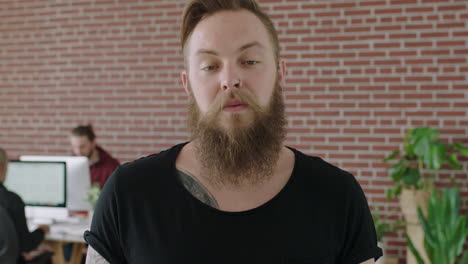 close-up-portrait-of-young-bearded-caucasian-man-entrepreneur-looking-serious-pensive-at-camera-focused-male-in-modern-workspace-background