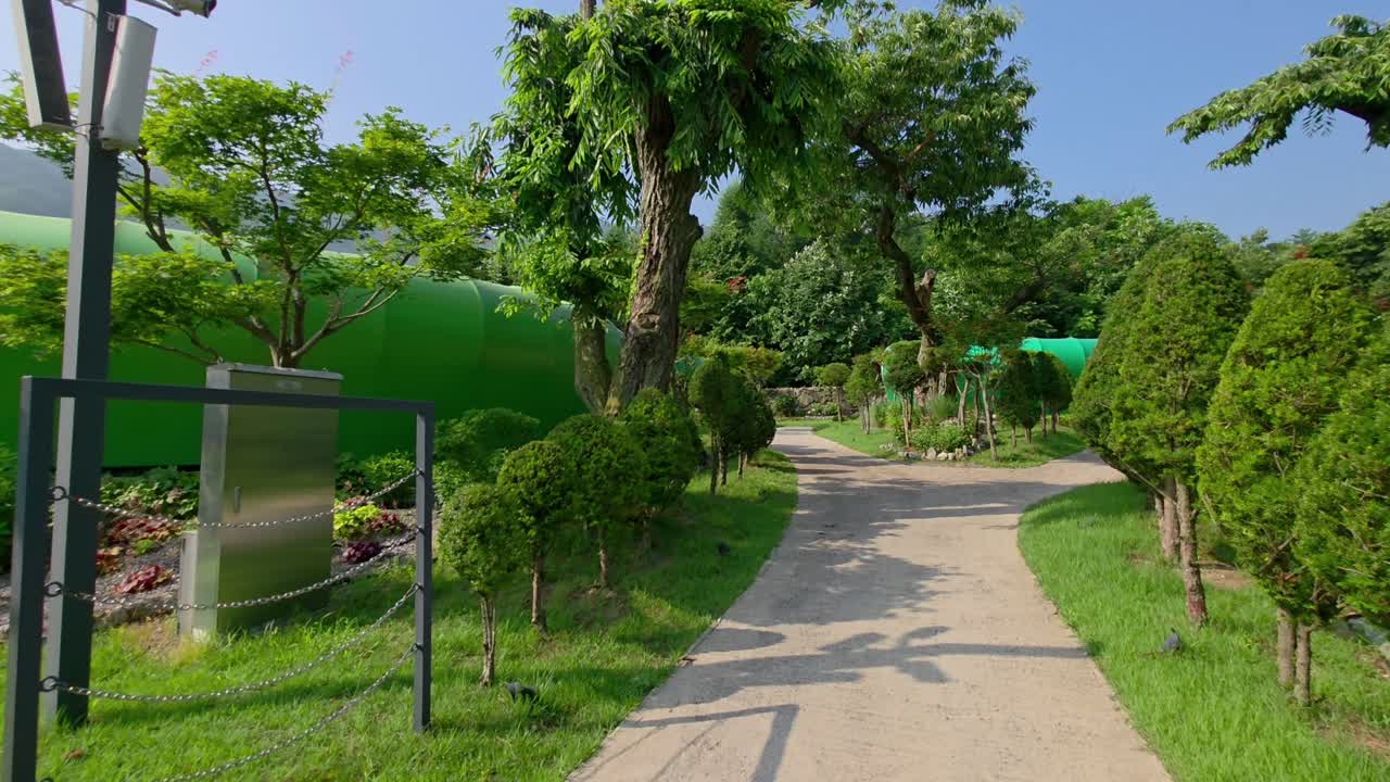 A point-of-view walk along winding garden paths at Glamtree Resort in Gapyeong, Korea, reveals manicured greenery, chestnut trees, and tranquil natural landscaping and leaf-shaped cabins