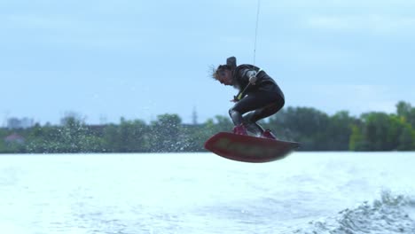 Male-wakeboarder-riding-on-river-in-wakeboard-jumping-high-above-water